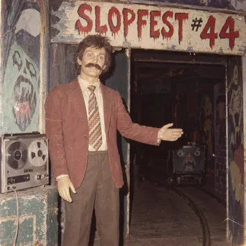 Flash-lit Instamatic snapshot: a mannequin with a real moustache at a ghost-train entrance, a painted sign above it: SLOPFEST #44